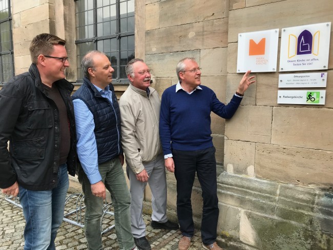 Vorstand MGK e.V. vor dem Schild der Dreifaltigkeitskirche Bad Berneck